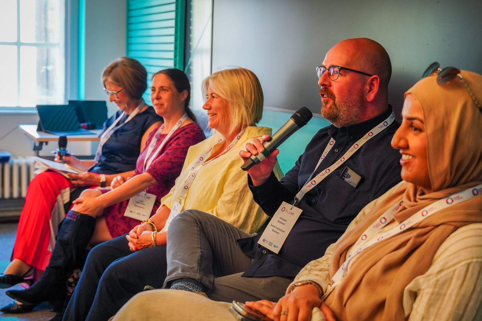 A panel of 5 people sitting, a man is holding the microphone
