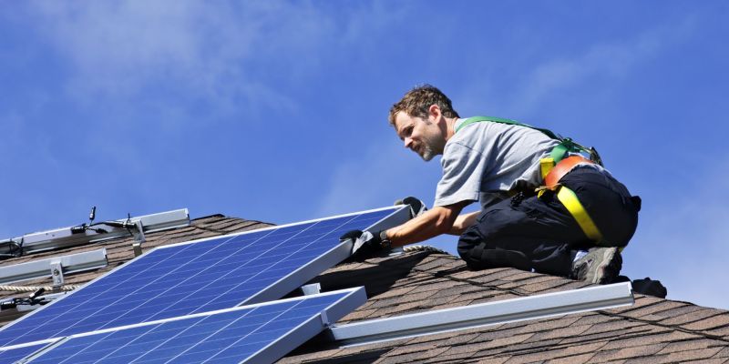 Someone securing solar panels to the top of a building