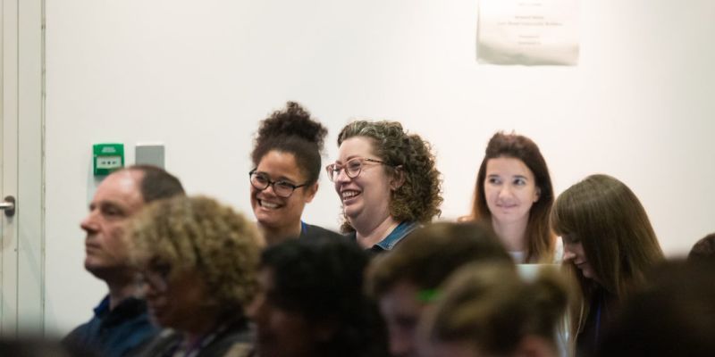 3 women amongst a group of people seated smiling